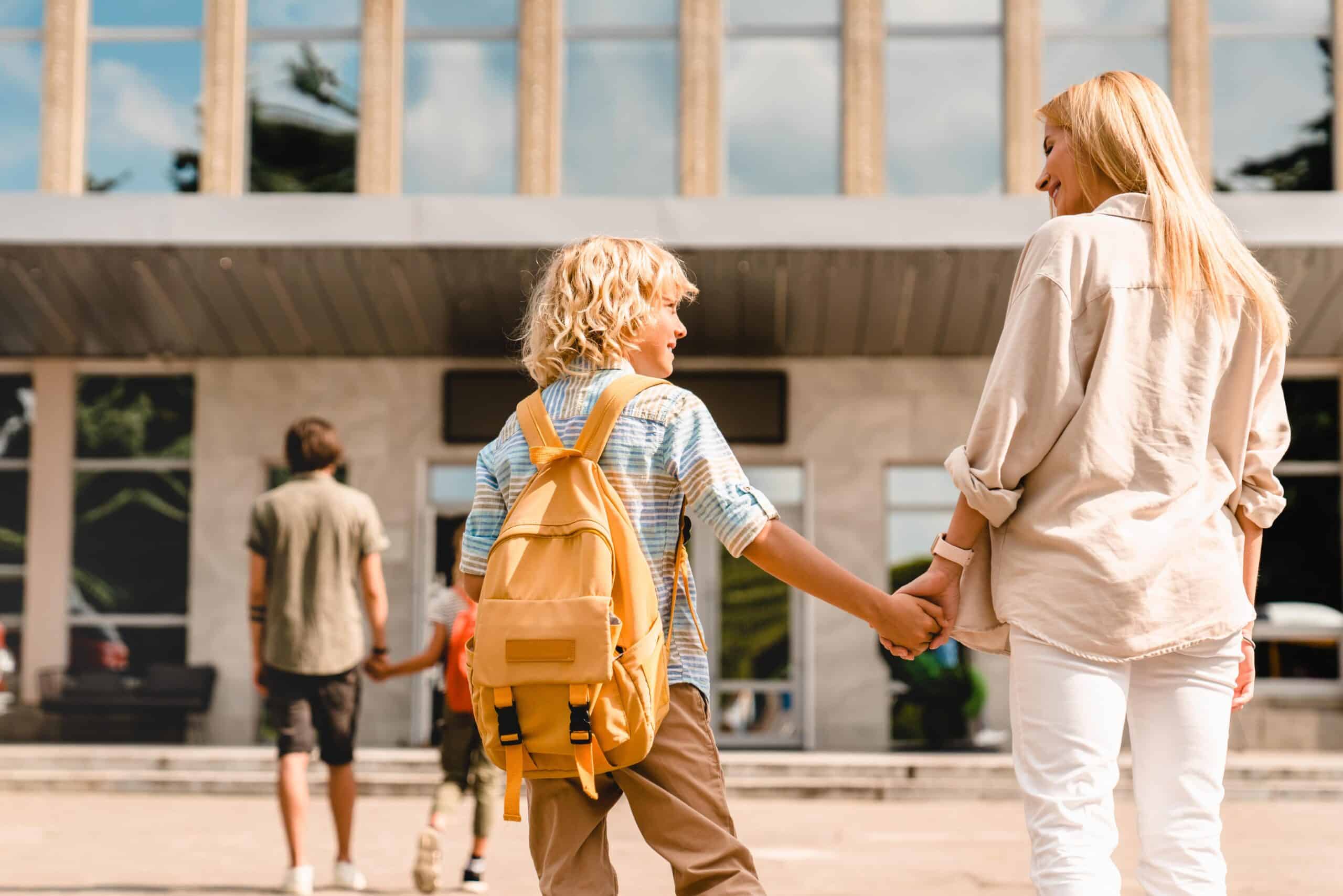 A young student holding hands with an adult outside a school building, symbolizing support and guidance—key aspects of SEN Teaching Assistant Jobs in Peterborough
