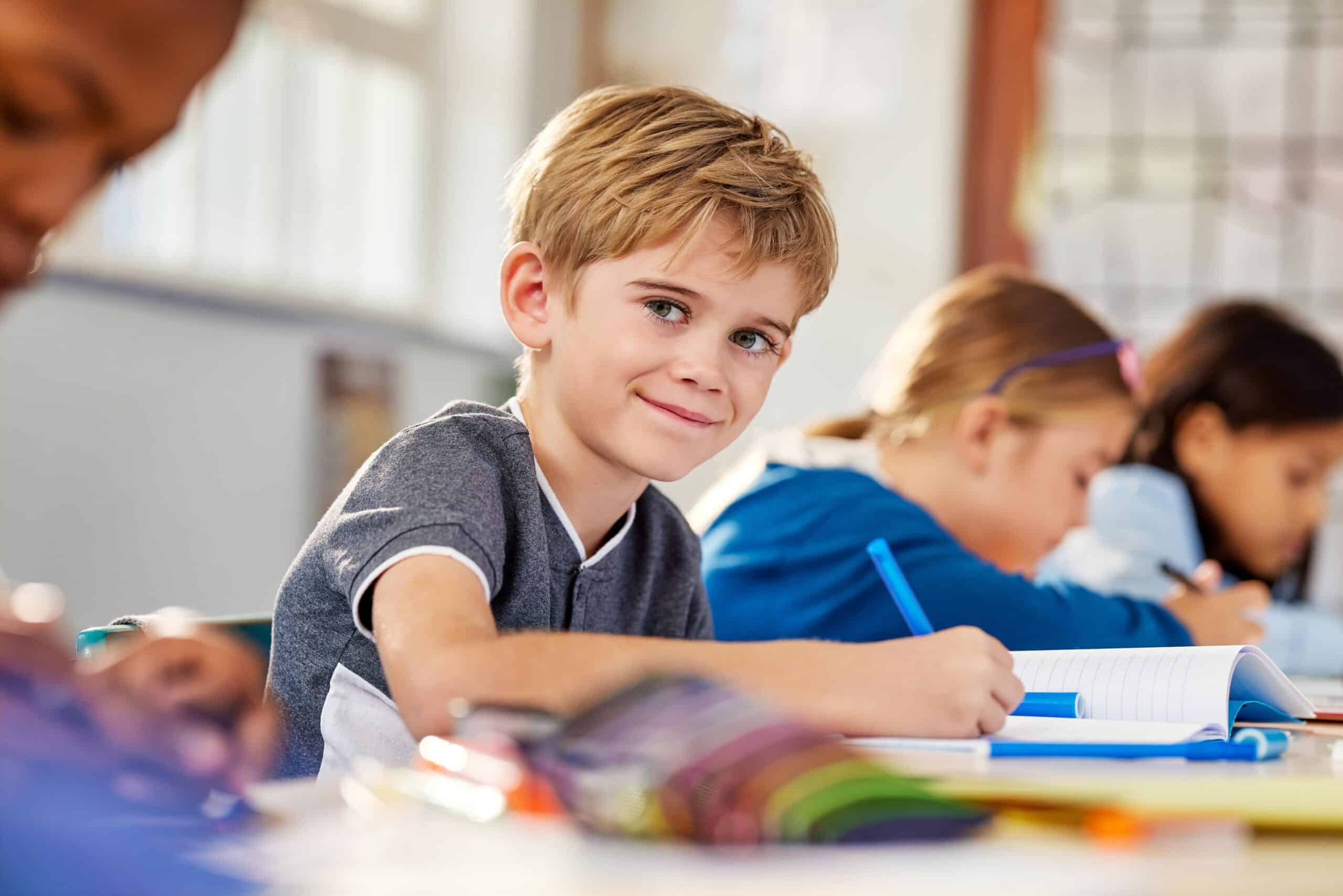 Smiling primary school pupil writing in a classroom, representing the supportive and inspiring environment created through Primary School Teacher Jobs in Peterborough